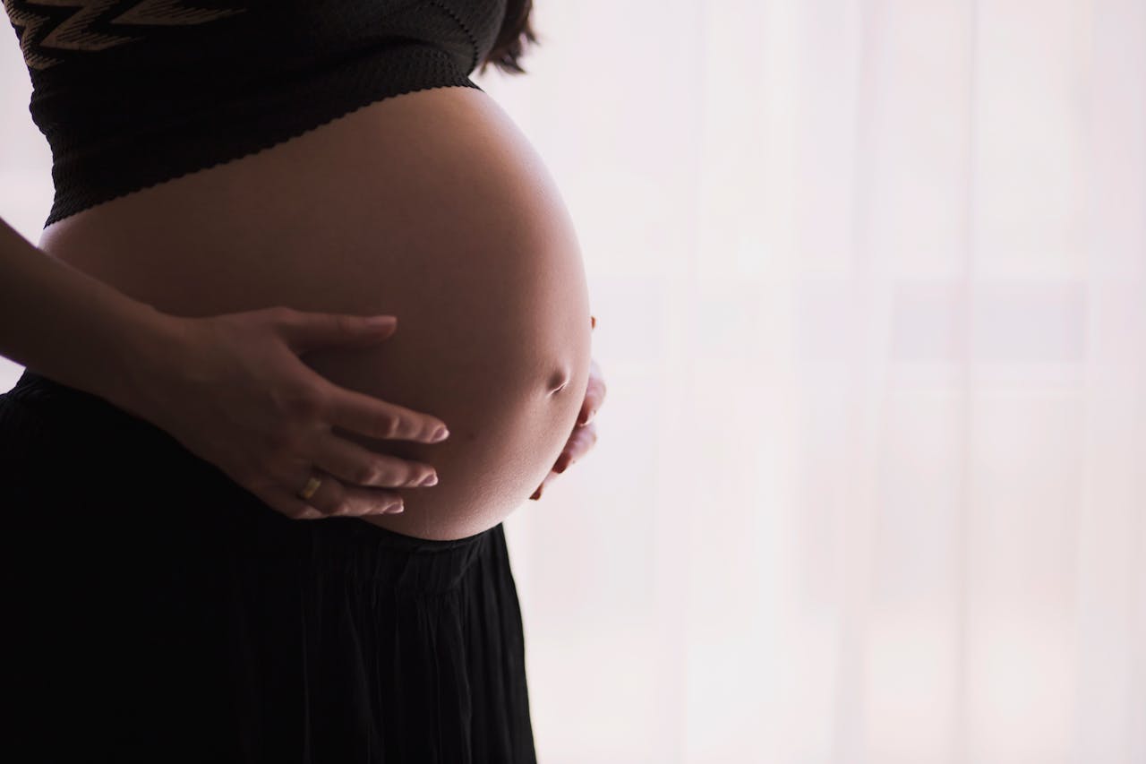 A close-up of a pregnant woman touching her bare belly, expressing warmth and care.